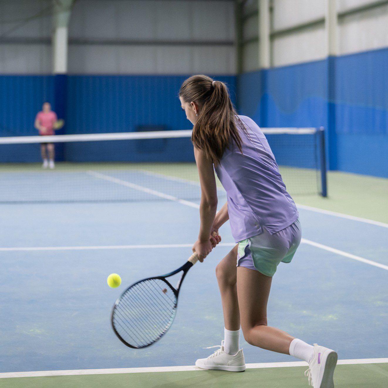 Woman playing tennis on indoor court.