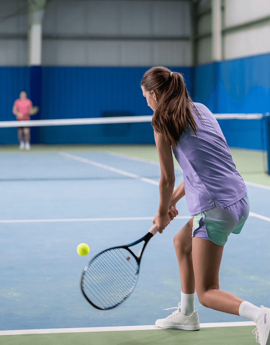 Woman playing tennis on indoor court.